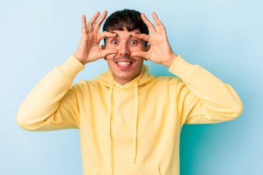 Genç melez adam mavi arka planda izole edildi. Başarı fırsatı bulmak için gözlerini açık tutuyor..