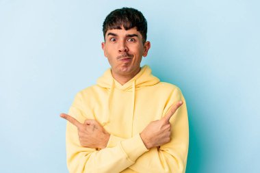 Genç melez adam mavi arka plan noktalarında izole edilmiş, iki seçenek arasında seçim yapmaya çalışıyor..