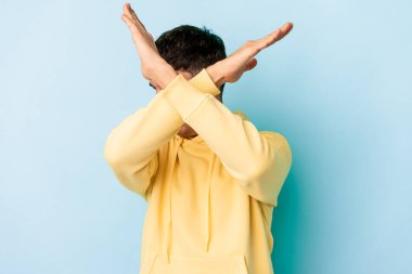 Genç melez adam mavi arka planda izole edilmiş iki kolu çapraz tutuyor, inkar kavramı..