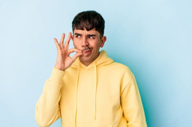 Genç melez adam mavi arka planda izole edilmiş ve parmakları dudaklarında bir sır saklıyor..