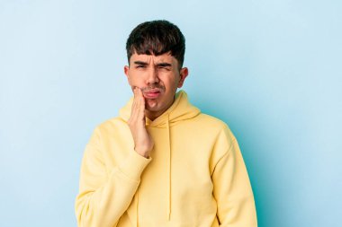 Genç melez adam mavi arka planda izole edilmiş güçlü bir diş ağrısı, azıdişi ağrısı var..