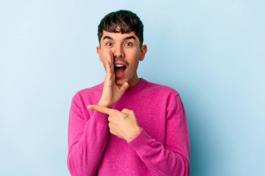 Genç melez adam mavi arka planda izole edilmiş. Dedikodu yapıyor, bir şeyleri bildiriyor..