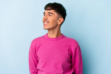 Genç melez adam mavi arka planda izole edilmiş gevşemiş ve mutlu bir şekilde gülüyor, boynunda dişler var..