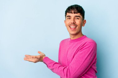 Genç melez adam mavi arka planda izole edilmiş bir şekilde avucunun içinde bir kopya alanı tutuyor..