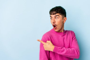 Genç melez adam mavi arka planda izole edilmiş, başparmak uzakta, gülüyor ve kaygısız..