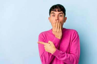 Genç melez adam mavi arka planda izole edilmiş, yan tarafı işaret ediyor.