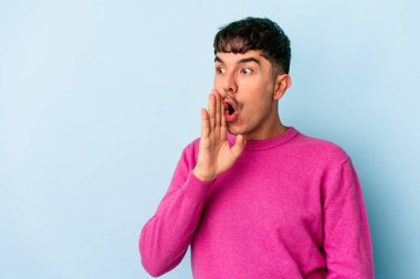 Genç melez adam mavi arka planda izole edildi. Gördüğü bir şey yüzünden şok oldu..