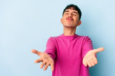 Genç melez adam mavi arka planda izole edilmiş dudaklar kıvrılıyor ve hava öpücüğü göndermek için avuç içi tutuyor..