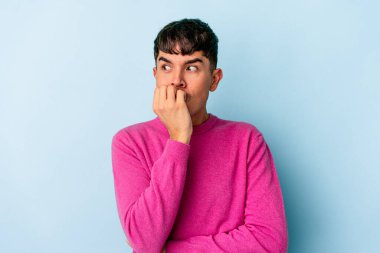 Genç melez adam mavi arka planda izole edilmiş tırnak yiyor, gergin ve çok endişeli..