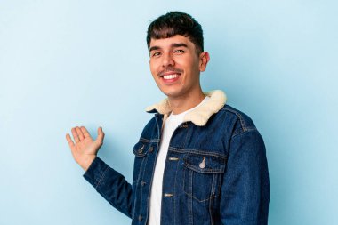 Mavi arka planda izole edilmiş genç melez bir adam hoş bir yüz ifadesi sergiliyor..