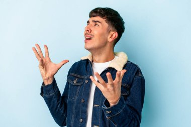 Genç melez adam mavi arka planda izole edilmiş gökyüzüne haykırıyor, yukarı bakıyor, hayal kırıklığına uğramış..