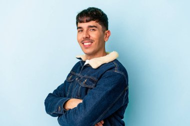 Genç melez adam mavi arka planda izole edilmiş kendinden emin, kararlılıkla kollarını kavuşturuyor..