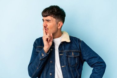 Genç melez adam mavi arka planda izole edilmiş bir şekilde sır saklıyor ya da sessizlik istiyor..