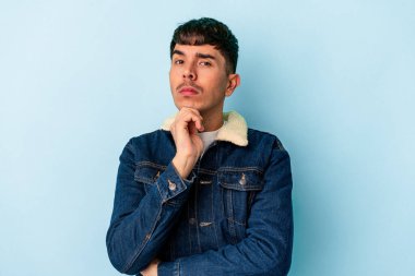 Genç melez adam mavi arka planda izole edilmiş şüpheli, belirsiz, seni inceliyor..