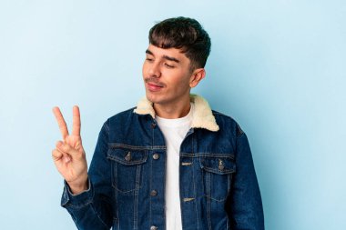 Genç melez adam mavi arka planda izole edilmiş neşeli ve tasasız parmakları olan bir barış sembolü gösteriyor..