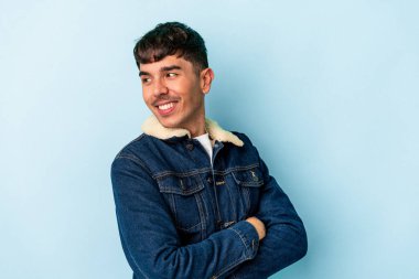 Genç melez adam mavi arka planda izole edilmiş gülüyor ve eğleniyor..