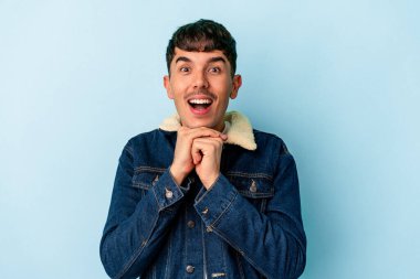Genç melez adam mavi arka planda izole edilmiş şans için dua ediyor, şaşırmış ve ağzı açık bir şekilde önüne bakıyor..