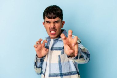 Mavi arka planda izole edilmiş genç melez bir adam pençelerini kedi taklidi yaparken gösteriyor, agresif bir hareket..