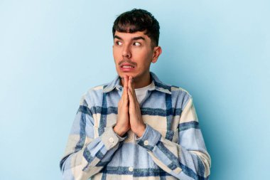 Genç melez adam mavi arka planda izole edilmiş dua ediyor, bağlılık gösteriyor, dindar biri ilahi ilham arıyor..