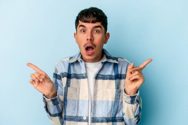 Genç melez adam mavi arka planda izole edilmiş farklı kopya alanlarını gösteriyor, birini seçiyor, parmaklarıyla gösteriyor.