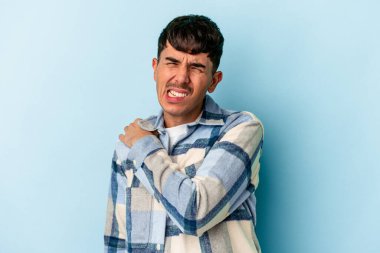 Genç melez adam, mavi arka planda izole edilmiş, omuz ağrısı çekiyor..
