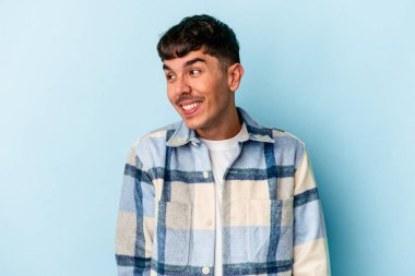 Genç melez adam mavi arka planda izole edilmiş gülüyor ve gözlerini kapıyor, rahatlamış ve mutlu hissediyor..