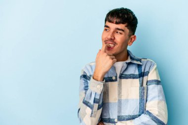 Genç melez adam mavi arka planda izole edilmiş rahat bir şekilde fotokopi odasına bakan bir şeyi düşünüyor..