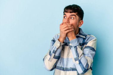 Genç melez adam mavi arka planda izole edilmiş. Düşünceli bir şekilde bir fotokopi odasına bakıyor. Ağzını eliyle kapatıyor..