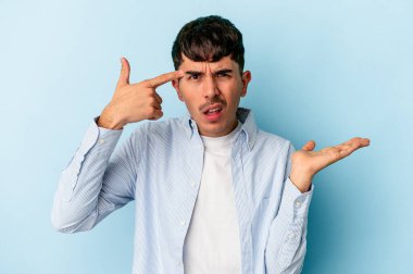 Genç melez adam mavi arka planda izole edilmiş işaret parmağıyla hayal kırıklığı jesti gösteriyor..
