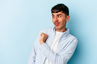 Genç melez adam mavi arka planda izole edilmiş kafası karışmış, şüpheli ve güvensiz hissediyor..