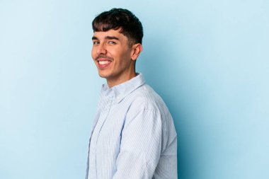 Genç melez adam mavi arka planda izole edilmiş. Kendine güvenen, ellerini kalçasında tutan..