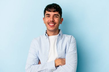 Genç melez adam mavi arka planda izole edilmiş kendinden emin, kararlılıkla kollarını kavuşturuyor..