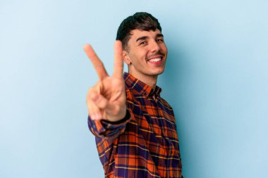 Genç melez adam mavi arka planda izole edilmiş neşeli ve tasasız parmakları olan bir barış sembolü gösteriyor..