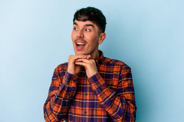 Genç melez adam mavi arka planda izole edilmiş şans için dua ediyor, şaşırmış ve ağzı açık bir şekilde önüne bakıyor..