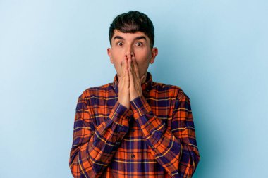 Genç melez adam mavi arka planda izole edilmiş ağzı kapalı ve elleri endişeli görünüyor..