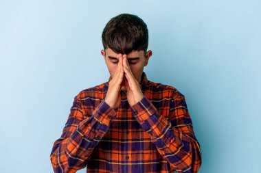 Genç melez adam mavi arka planda izole edilmiş dua ediyor, bağlılık gösteriyor, dindar biri ilahi ilham arıyor..