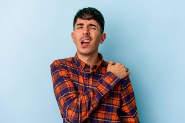 Genç melez adam, mavi arka planda izole edilmiş, omuz ağrısı çekiyor..