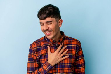 Mavi arka planda soyutlanmış genç melez adam yüksek sesle gülüyor elini göğsüne koyuyor..