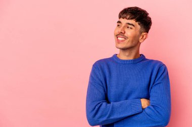 Pembe arka planda soyutlanmış genç melez adam kollarını kavuşturarak gülümsüyor..