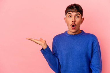 Pembe arka planda izole edilmiş genç melez adam, avuç içinde kopya alanı tutmaktan etkilenmiş..