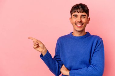 Pembe arka planda izole edilmiş genç melez adam işaret parmağıyla işaret ederek gülümsüyor..