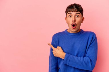 Genç melez adam, pembe arka planda izole edilmiş, kenarı işaret ediyor.