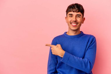 Genç melez adam pembe arka planda izole edilmiş gülümseyen ve işaret eden boş alanda bir şey gösteriyor..