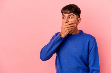 Genç melez adam pembe arka planda izole edilmiş. Düşünceli bir şekilde bir fotokopi odasına bakıyor. Ağzını eliyle kapatıyor..