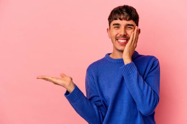 Pembe arka planda izole edilmiş melez genç bir adam avuç içinde fotokopi alanı tutuyor, el üstünde tutuyor. Şaşırmış ve mutlu..