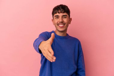 Genç melez adam pembe arka planda izole edilmiş kameraya elini uzatarak selam veriyor..