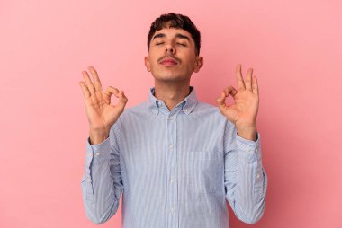 Genç melez adam pembe arka planda izole edilmiş sıkı çalışma gününden sonra rahatlıyor, yoga yapıyor..