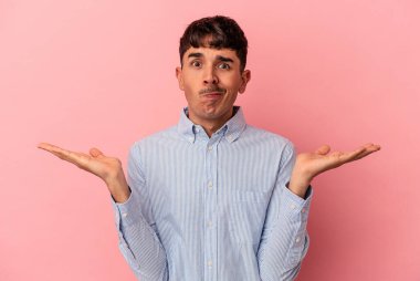 Genç melez adam pembe arka planda izole edilmiş. Kafası karışmış ve omuz silkiyor. Kopya alanını tutmak için..