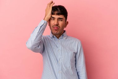 Genç melez adam pembe arka planda izole edilmiş. Çok yorgun ve uykulu. Elini başının üstünde tutuyor..