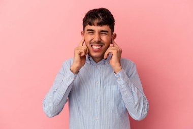 Genç melez adam pembe arka planda izole edilmiş kulakları elleriyle kapatıyor..
